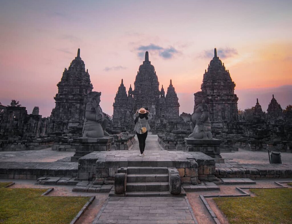Yang baru belum tentu diburu yang usang terkadang lebih di sayangSunset Candi SewuLokasi - Ca - Mabur.co Person wearing a wide-brimmed hat walks toward towering ancient stone temples at sunset, within a historic ruin complex.