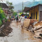 A flooded village street where people are shoveling mud and removing debris together after a flood (community cleanup).