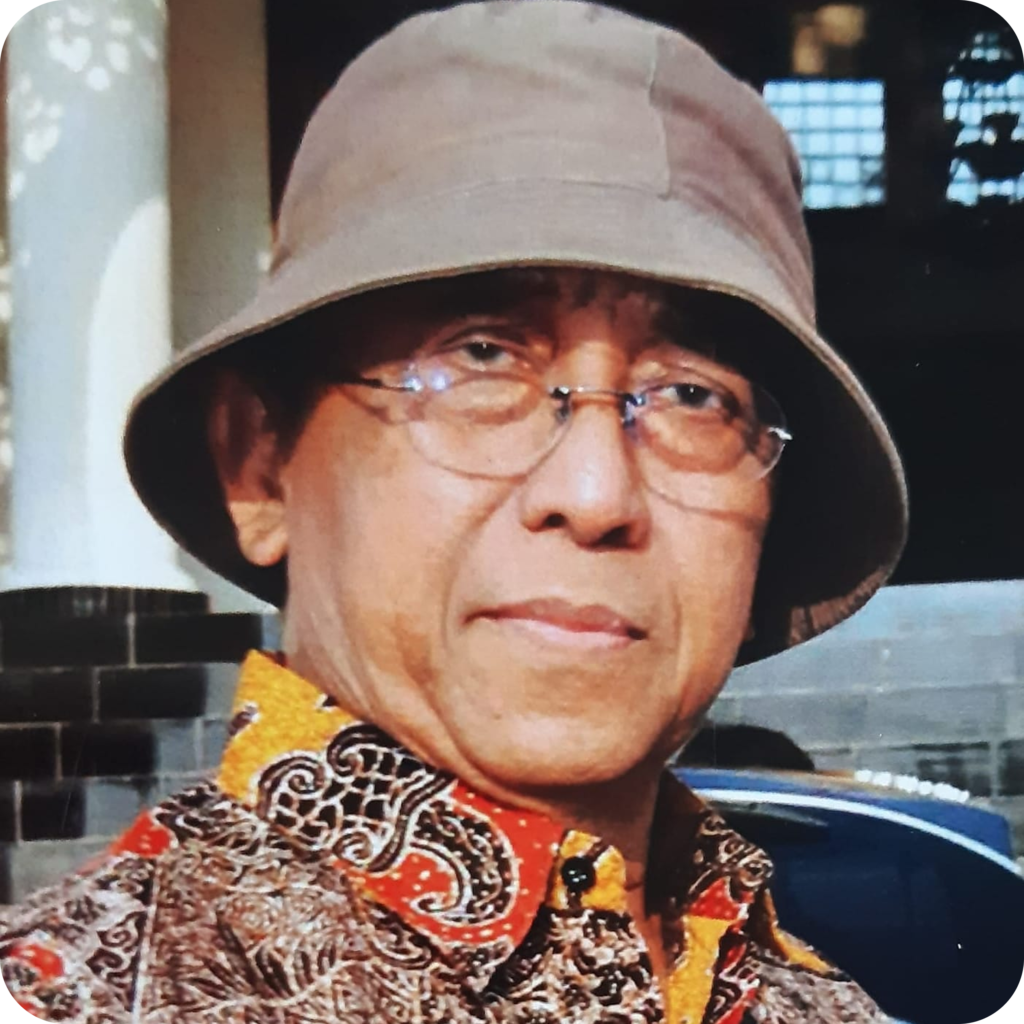 Portrait of a man wearing a beige bucket hat, glasses, and a colorful patterned shirt, looking at the camera.