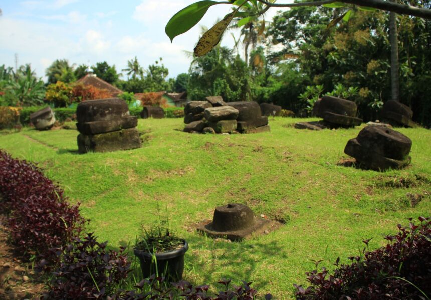 a75e9801c9d3ffd357c9cf9a4b251282 - Mabur.co Open grassy yard with large weathered stone blocks arranged in irregular piles, tropical plants in the background.