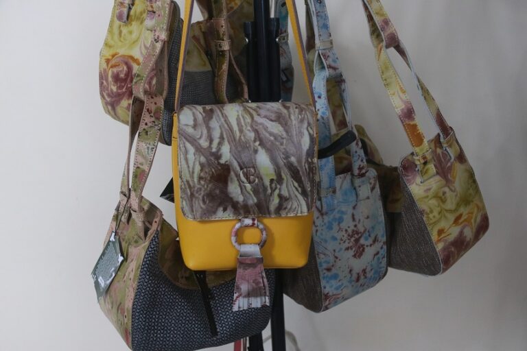 Assorted patterned handbags hanging on a display stand, including a yellow front bag with a marble flap.