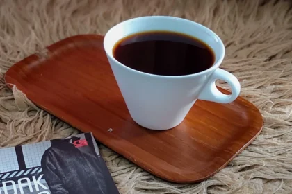 White coffee cup filled with dark coffee sits on a wooden tray on a shaggy beige rug, with a magazine partially visible in the corner.