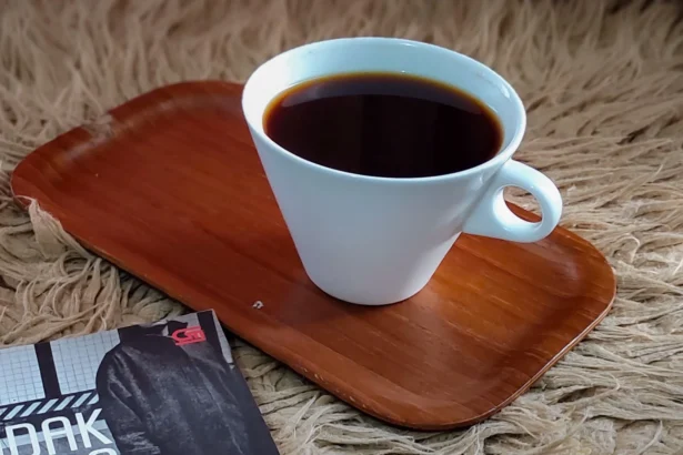 White coffee cup filled with dark coffee sits on a wooden tray on a shaggy beige rug, with a magazine partially visible in the corner.