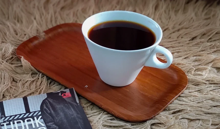 White coffee cup filled with dark coffee sits on a wooden tray on a shaggy beige rug, with a magazine partially visible in the corner.