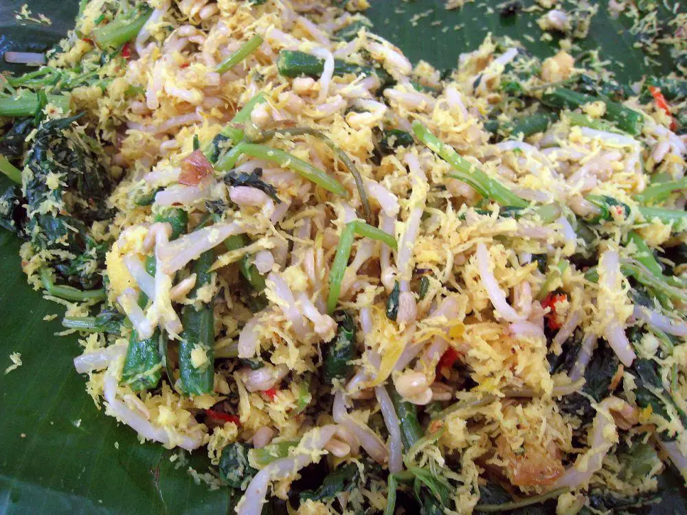 Shredded egg and vegetable dish with greens, bean sprouts, and peanuts on a banana leaf