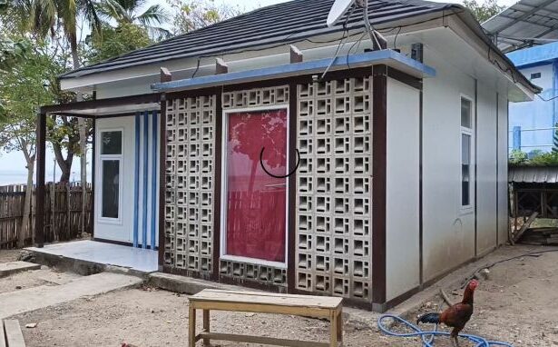Small white, single-story house with a decorative concrete lattice screen over the red front door, in a dirt yard with a rooster nearby.
