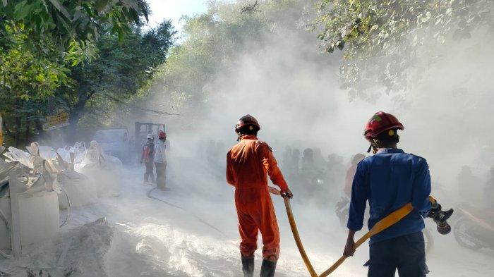 Firefighters in orange and blue protective gear spraying water through a hose in a smoke-filled street during a fire event.