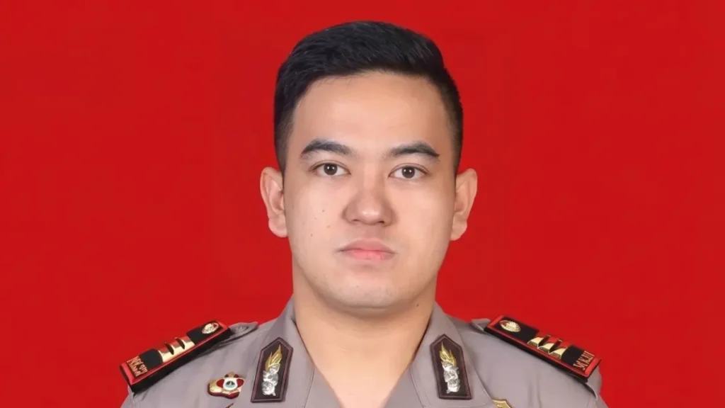 Portrait of a male police officer in uniform with insignia and medals against a solid red background.