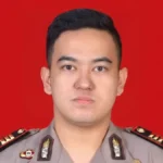 Portrait of a male police officer in uniform with insignia and medals against a solid red background.