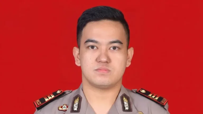 Portrait of a male police officer in uniform with insignia and medals against a solid red background.