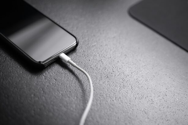 Close-up of a smartphone on a textured surface with a white charging cable connected to its bottom edge.