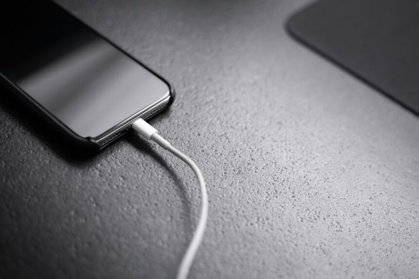 Close-up of a smartphone on a textured surface with a white charging cable connected to its bottom edge.