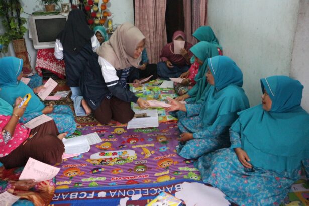 Group of women in turquoise outfits sitting on a colorful floor mat, exchanging papers.