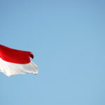 Indonesian flag waving from a flagpole against a clear blue sky.