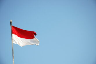 Indonesian flag waving from a flagpole against a clear blue sky.