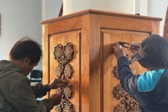 Two people attaching decorative star-shaped wooden inlays to a tall wooden cabinet or lectern, using tools on the panels.