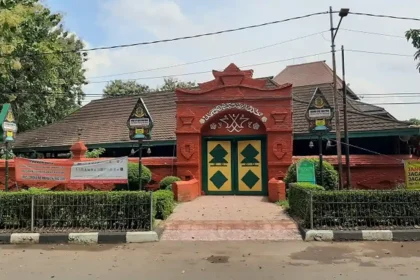 Red ornate gateway entrance to a compound with green-and-yellow double doors and banners along the fence.