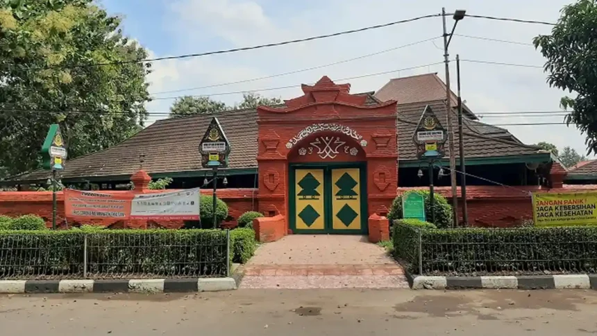 Red ornate gateway entrance to a compound with green-and-yellow double doors and banners along the fence.