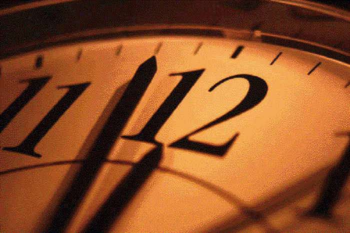 Close-up of a clock face with hands near 12 o'clock, bathed in warm amber lighting.
