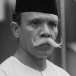 Portrait of a man with a curled white mustache, wearing a black fez and a white traditional shirt, looking to the side