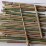 Assorted bamboo sticks laid out in parallel on a tiled floor, with one long bamboo pole crossing them diagonally.