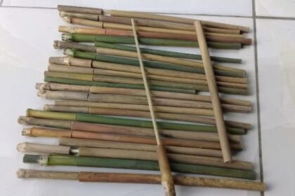Assorted bamboo sticks laid out in parallel on a tiled floor, with one long bamboo pole crossing them diagonally.