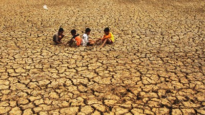 Five children sit on parched, cracked earth in a drought-stricken landscape with a dusty horizon periphery.