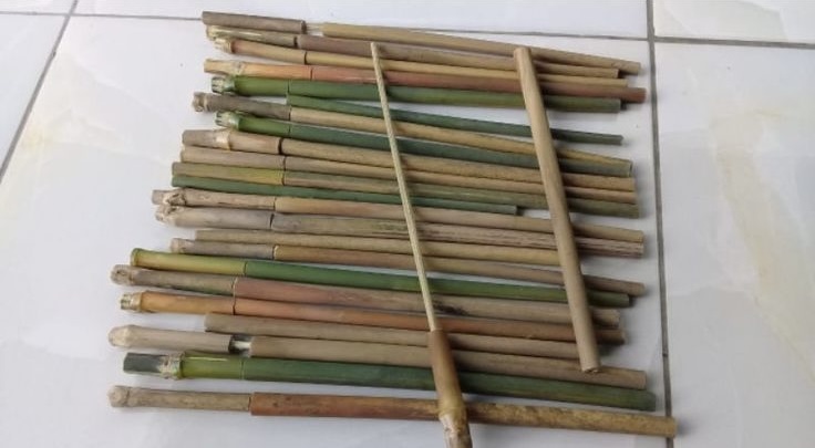 Assorted bamboo sticks laid out in parallel on a tiled floor, with one long bamboo pole crossing them diagonally.