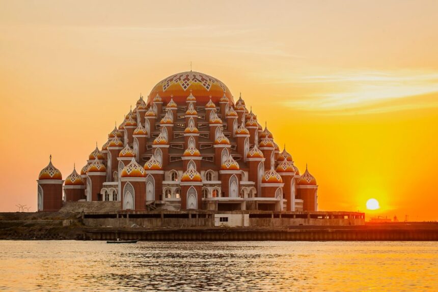 Sunset over a large lotus-shaped temple complex with orange domes by a calm river.