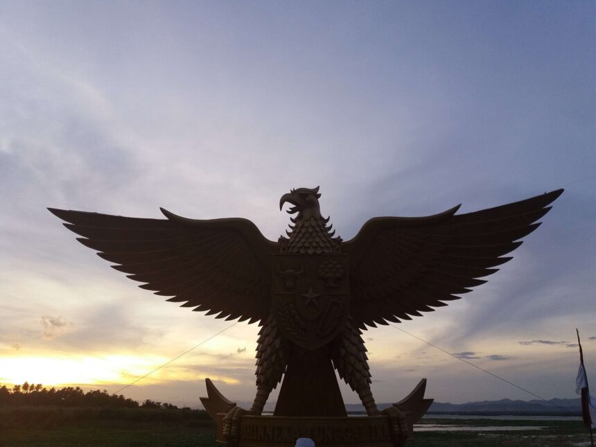 az - Mabur.co Silhouette of a large eagle statue with outstretched wings at sunset.