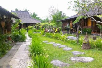 Tropical garden path with stepping stones, green lawn, and wooden cottages on either side.