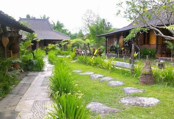 Tropical garden path with stepping stones, green lawn, and wooden cottages on either side.