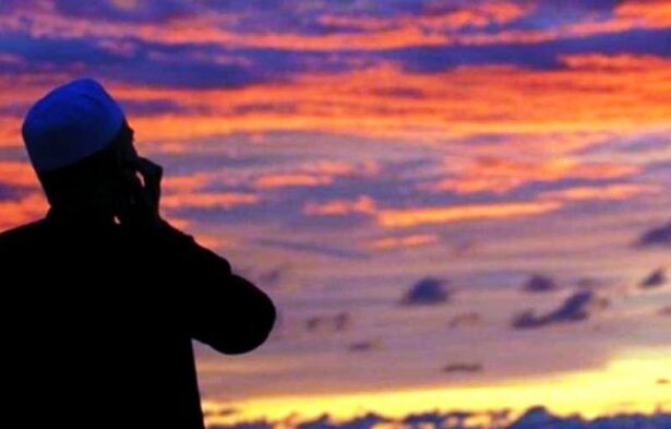 Silhouette of a man talking on a mobile phone against a vibrant sunset sky with orange and purple clouds.