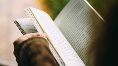 Close-up of hands holding and turning the pages of an open book, bathed in warm natural light