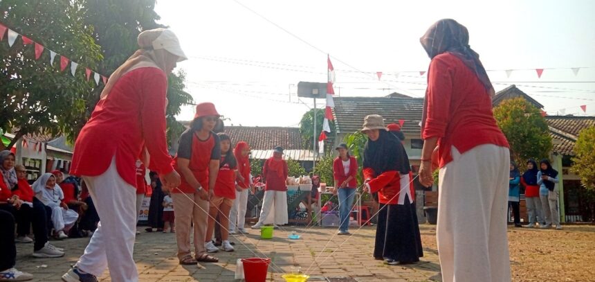 Group of people in red shirts playing a cup-and-string telephone game outdoors at a community event.