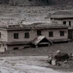 A partially buried, damaged two-story house surrounded by mud and debris after a flood or landslide.