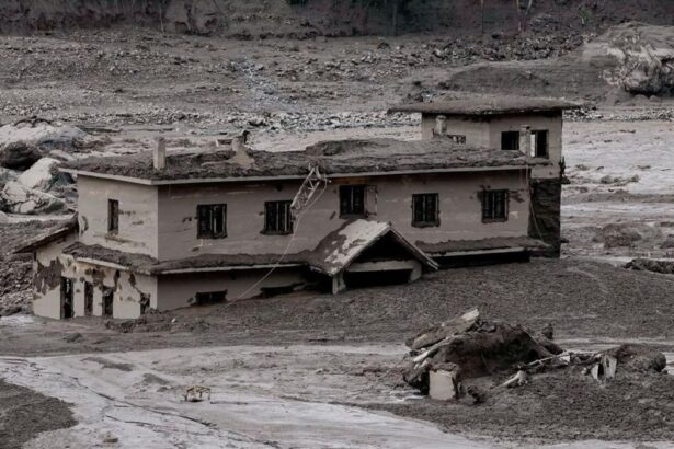 A partially buried, damaged two-story house surrounded by mud and debris after a flood or landslide.