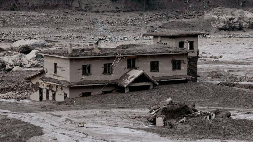 A partially buried, damaged two-story house surrounded by mud and debris after a flood or landslide.