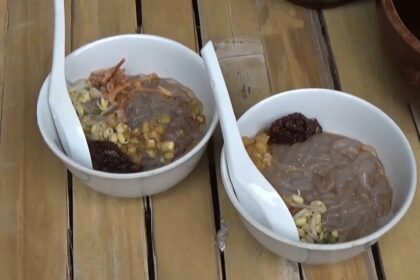 Two white bowls on a wooden table containing raw meat with pasta and vegetables, arranged for cooking or serving.