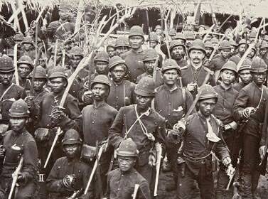 Black-and-white photo of a large group of soldiers in vintage uniforms holding rifles, posing for a military portrait in a dense formation.