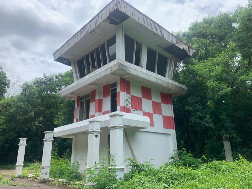 Abandoned two-story lookout tower with a red-and-white checkerboard exterior in a overgrown, wooded area.
