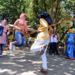 Group of women and girls skipping rope in a sunny park surrounded by trees.