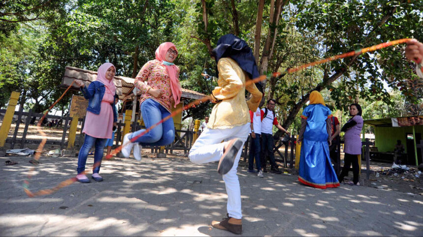 bermain tali by tempo co - Mabur.co Group of women and girls skipping rope in a sunny park surrounded by trees.