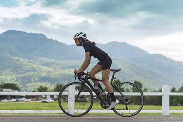 Woman cyclist wearing a white helmet and black kit riding a road bike along a rural road with mountains in the background.