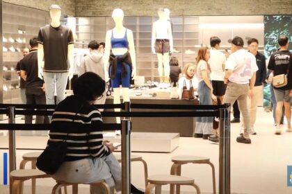 Shoppers browse a clothing store with mannequins on display and a person sitting in the foreground wearing a striped sweater.