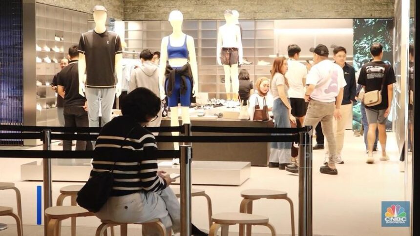 Shoppers browse a clothing store with mannequins on display and a person sitting in the foreground wearing a striped sweater.