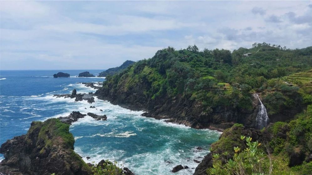 bukit pengilon by Nagantour com - Mabur.co Coastline with rocky cliffs, lush green hillside, and a small waterfall cascading into the turquoise sea. (informative)