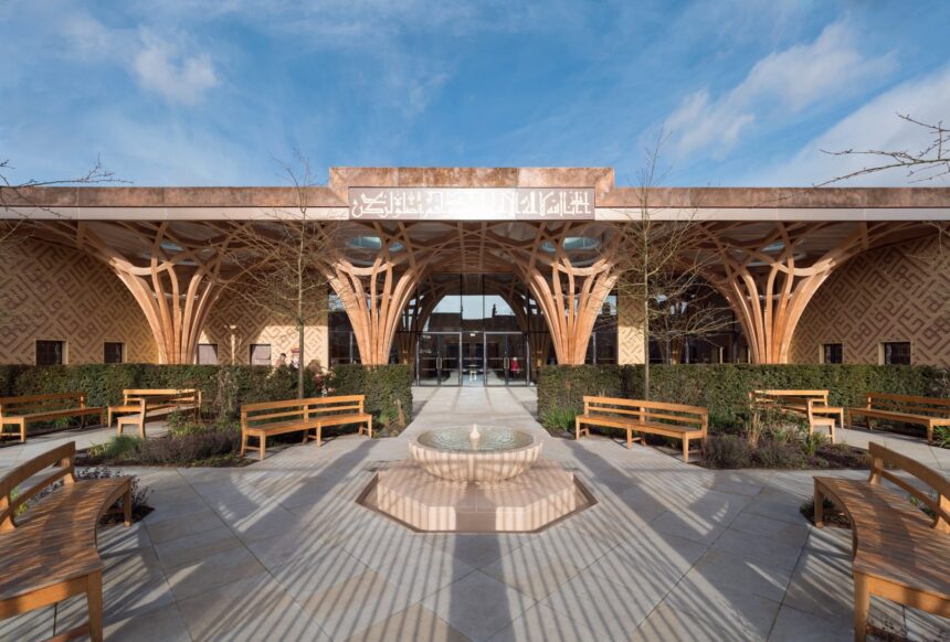 Symmetrical courtyard with curved wooden arches, benches, and a circular fountain in front of a building with Arabic signage under a blue sky.
