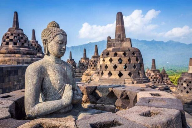 Stone Buddha statue in meditation at Borobudur, surrounded by bell-shaped stupas and stone terraces against a blue sky and distant hills