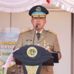 Uniformed official delivering a speech at a podium with a globe emblem and medals on his chest.